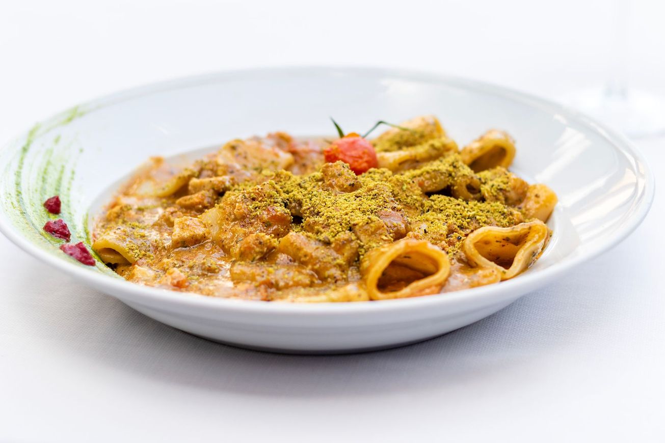 Piatto di pasta con salsa, pomodorini e pistacchi in una ciotola bianca.