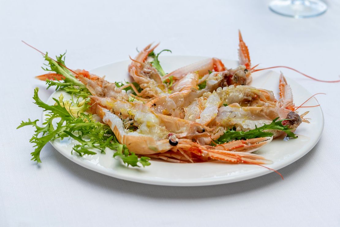 Piatto di scampi cotti con lattuga verde su una tovaglia bianca.