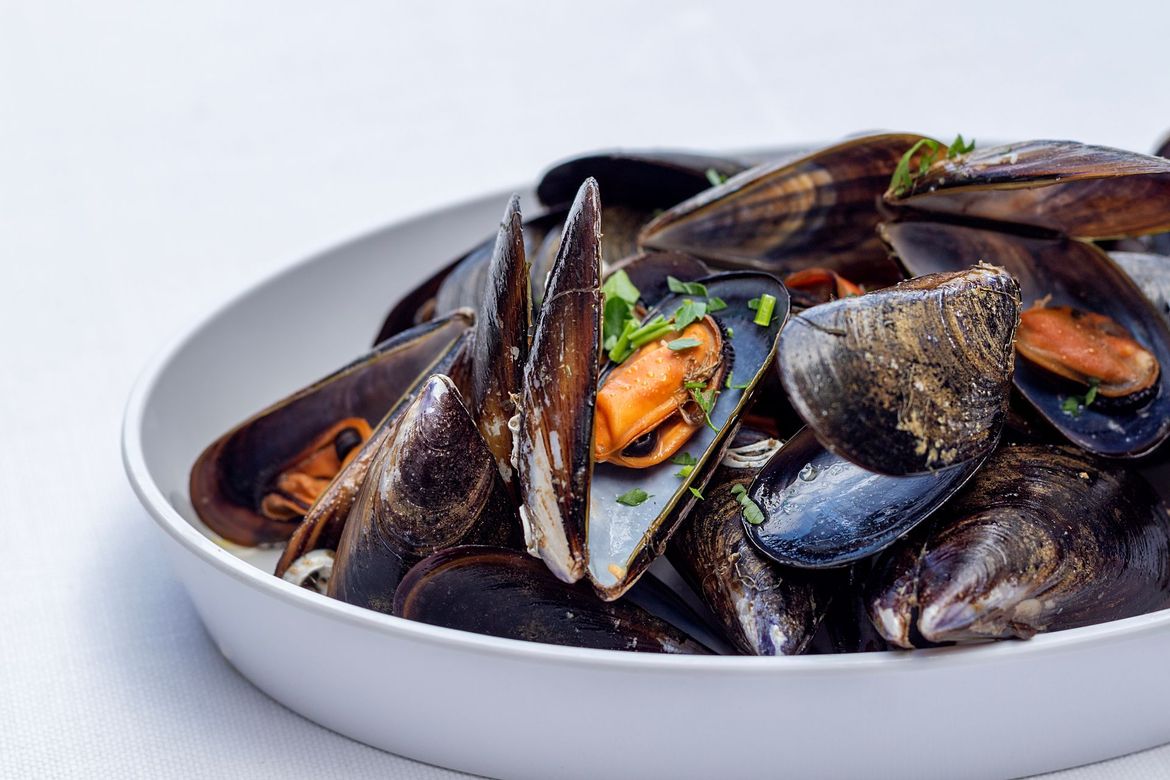 Cozze fumanti in una ciotola bianca, guarnite con erbe fresche.