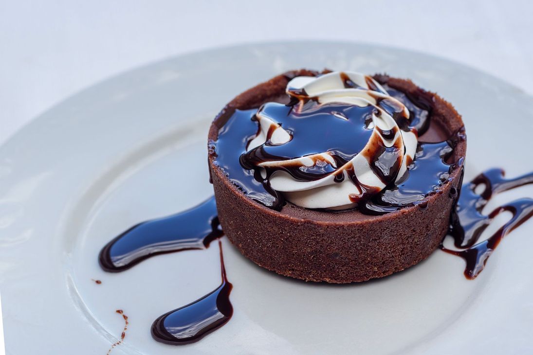 Crostata al cioccolato con panna montata e salsa al cioccolato su un piatto bianco.