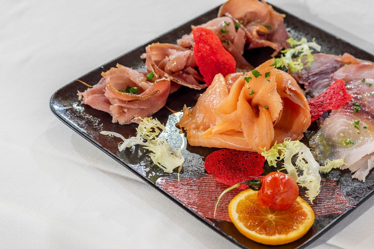 Piatto di antipasto con salumi, salmone, pesce, fetta d'arancia e frutti rossi.