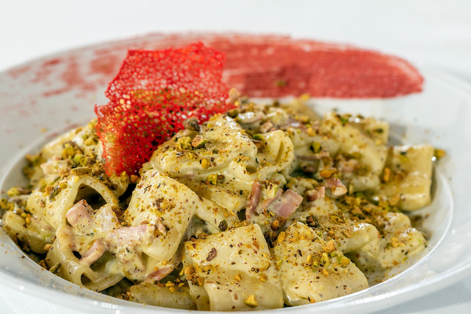 Piatto di pasta con salsa cremosa, pistacchi e guarnizione rossa in una ciotola bianca.