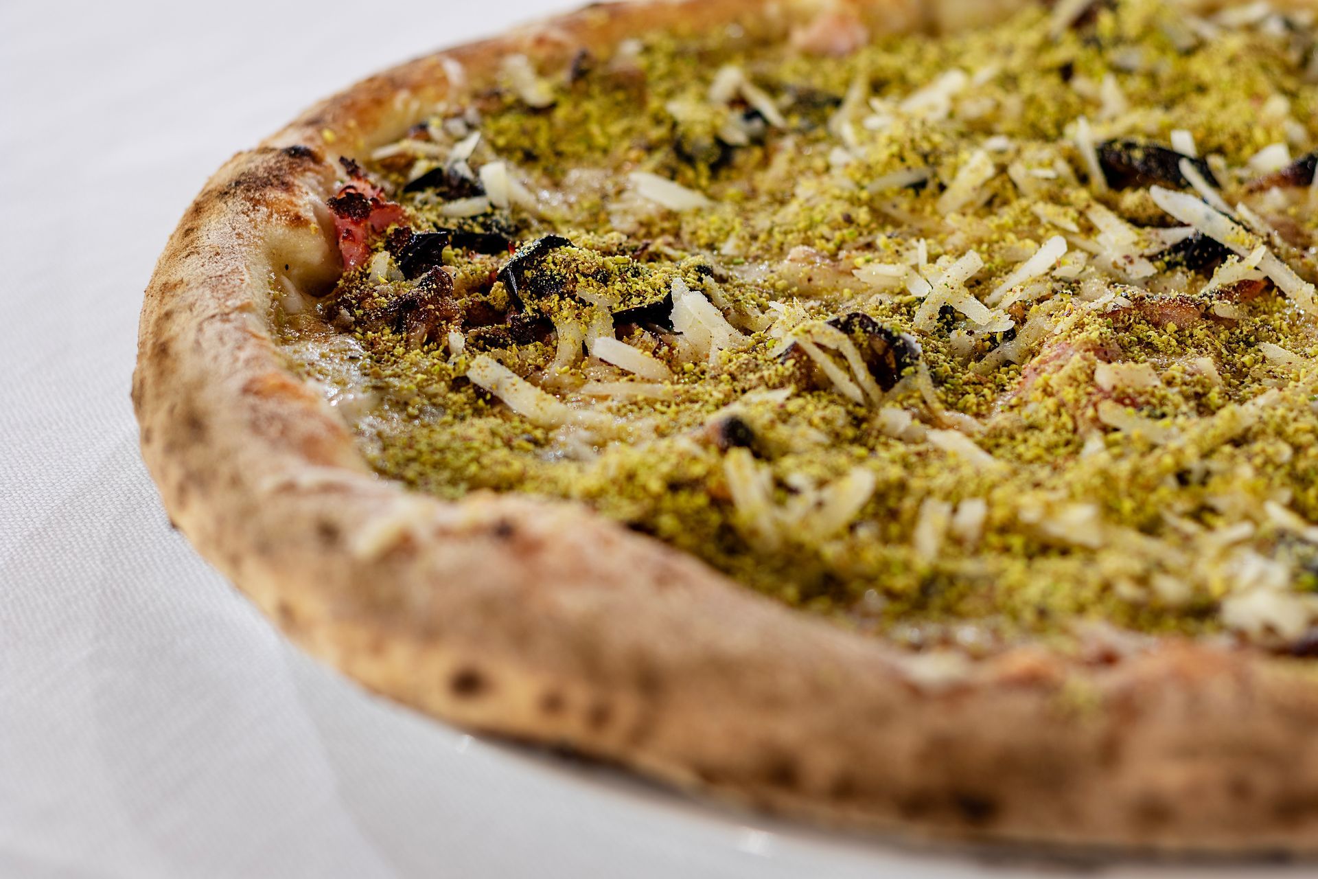 Pizza con ingredienti verdi e formaggio su un piatto bianco.