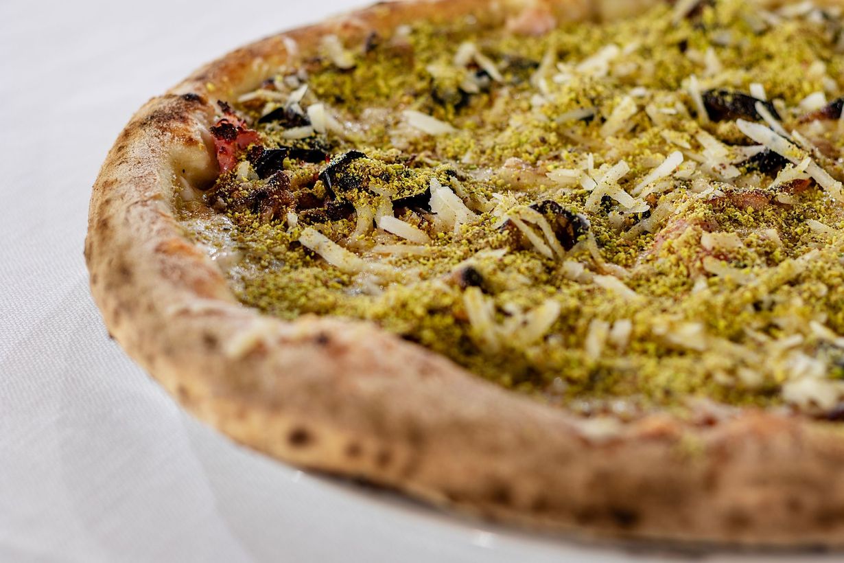 Pizza con ingredienti verdi e formaggio su un piatto bianco.