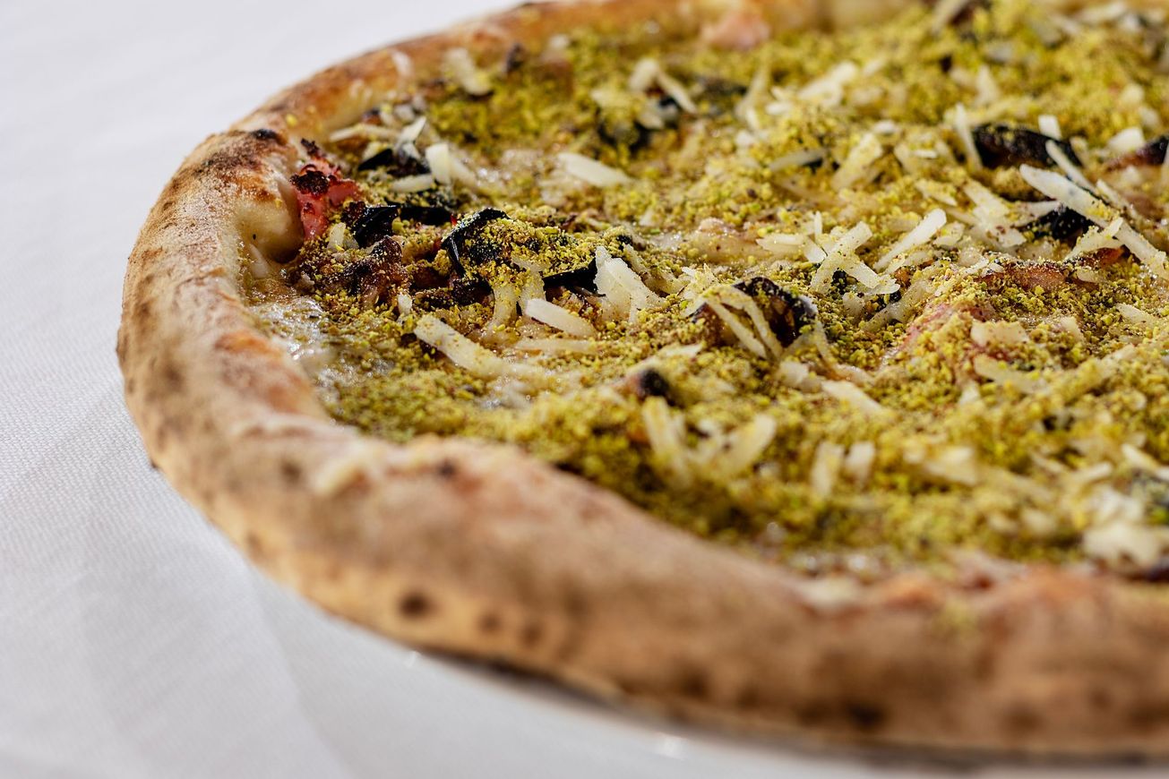 Pizza con ingredienti verdi e formaggio su un piatto bianco.