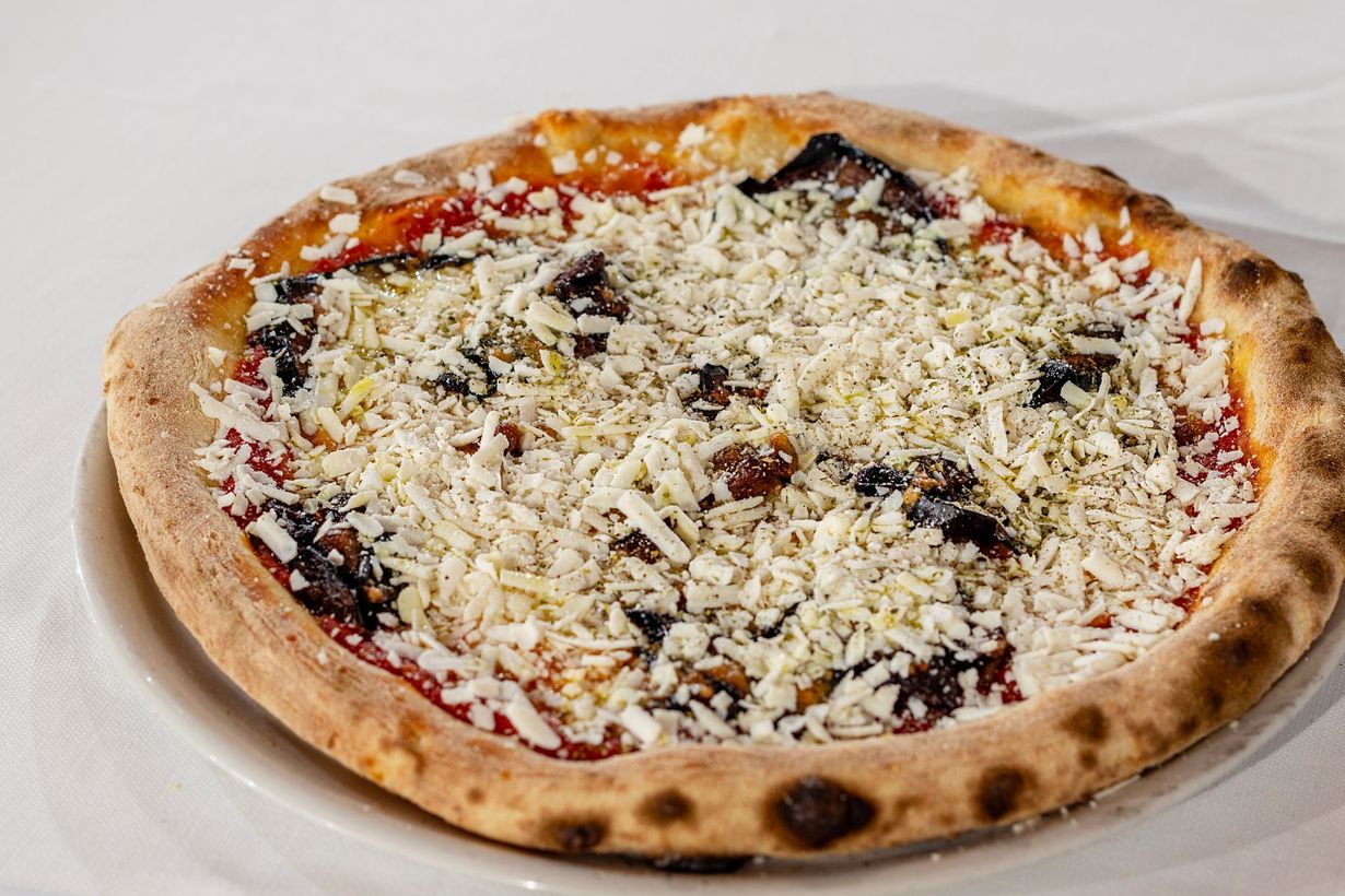 Pizza con crosta spessa, condita con salsa, funghi e formaggio bianco grattugiato, servita su un piatto bianco.