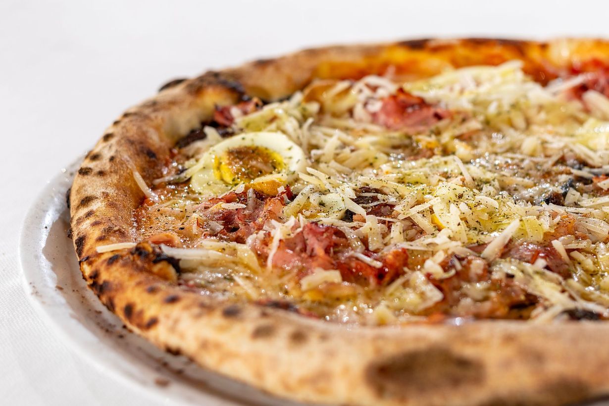 Pizza con condimenti, tra cui uova, prosciutto e formaggio, su un piatto bianco.