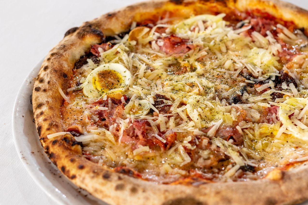 Pizza con base e condimenti tra cui uova, prosciutto e formaggio grattugiato.