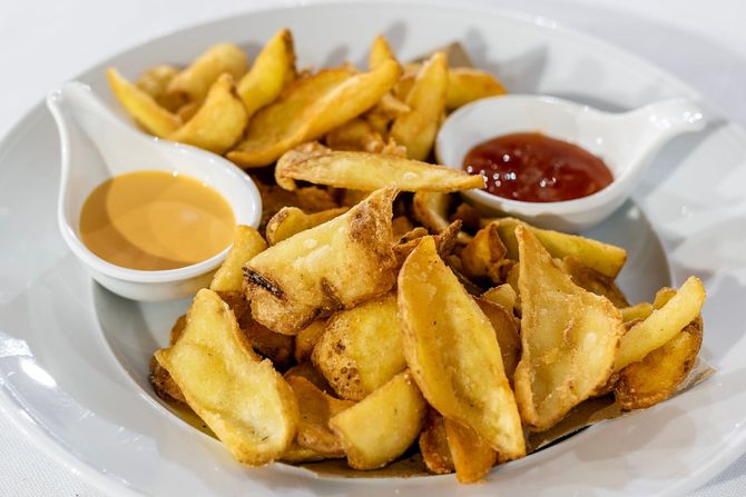 Piatto di spicchi di patate con due piccole salse, una all'arancia e una rossa.
