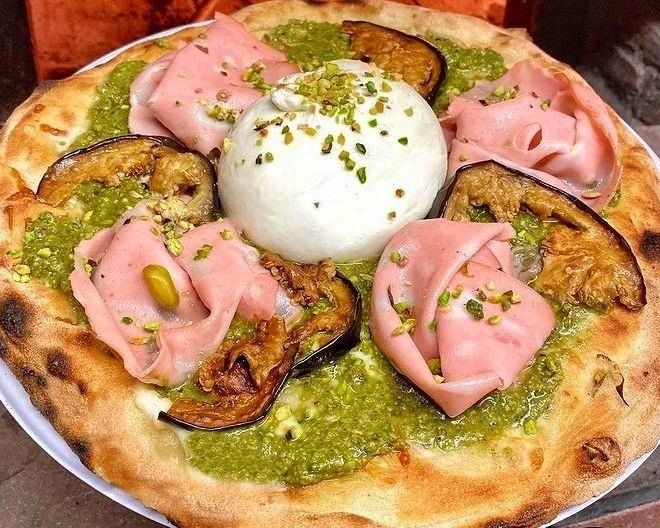 Pizza condita con pesto, mortadella, melanzane, burrata e pistacchi.