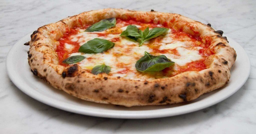 Pizza napoletana su piatto bianco, con salsa di pomodoro, mozzarella e basilico.