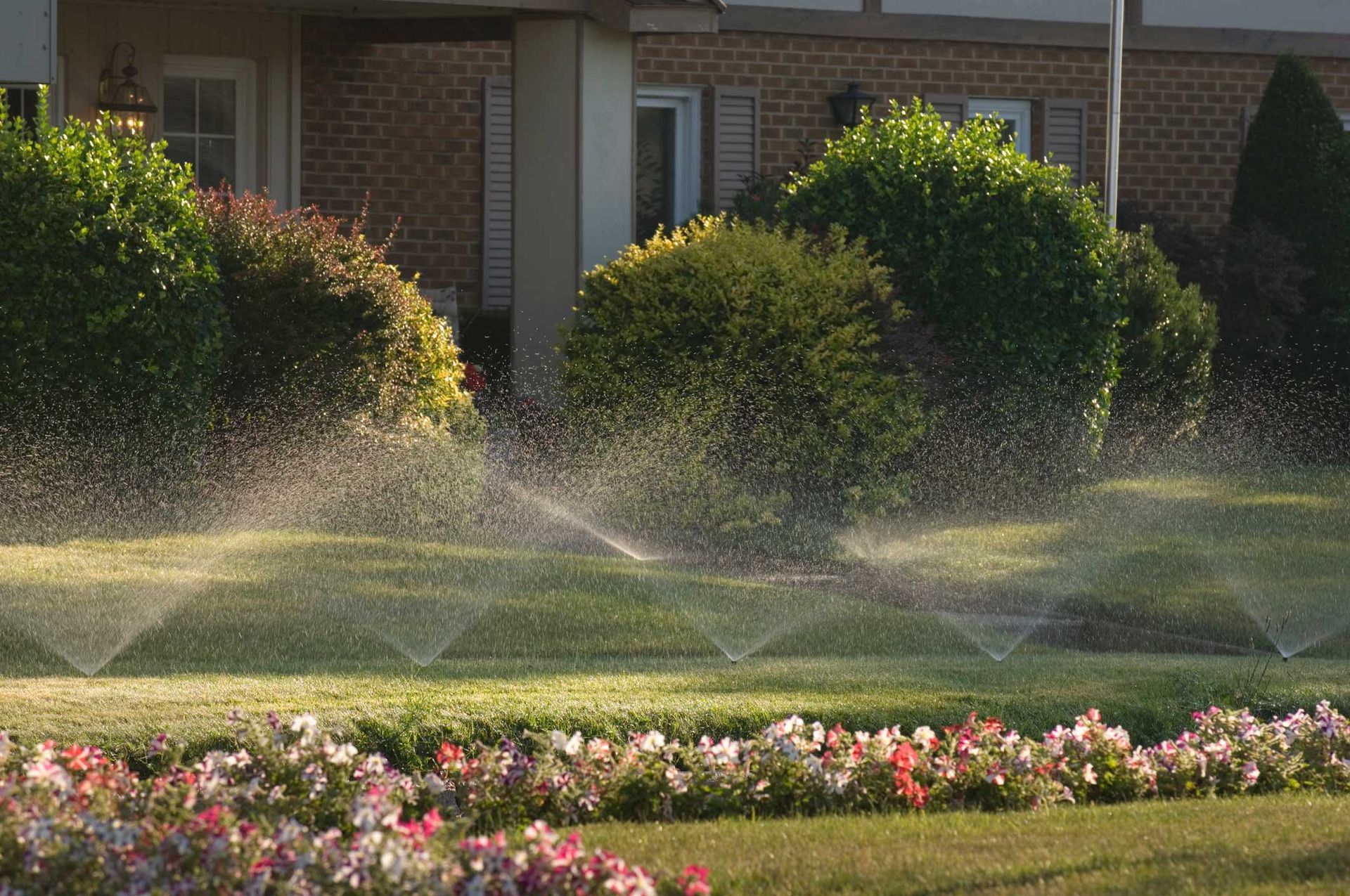 A sprinkler is spraying water on a lush green lawn in front of a house.
