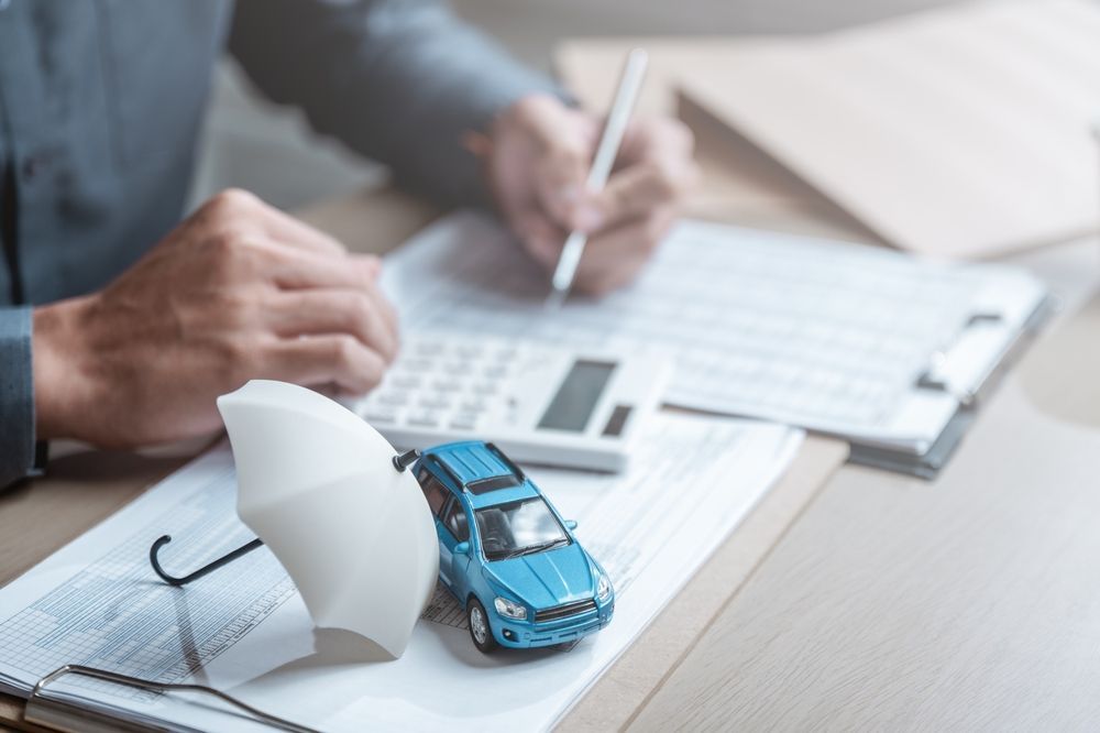 Hands reviewing paperwork beside a blue toy car on a desk with calculator and papers.