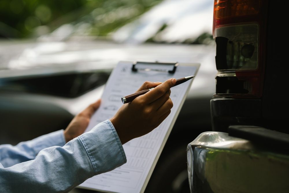 Hand holding a clipboard and pen next to a parked vehicle, inspecting a checklist.