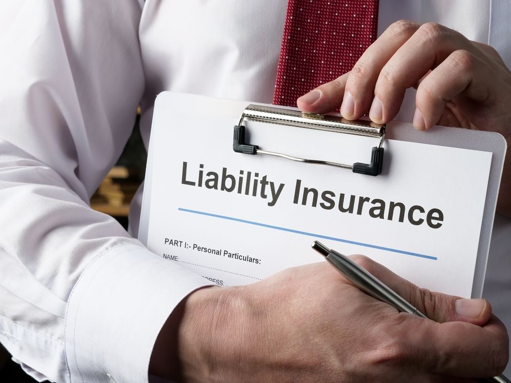 Hands holding a clipboard labeled “Liability Insurance” with a pen on a white shirt and red tie.