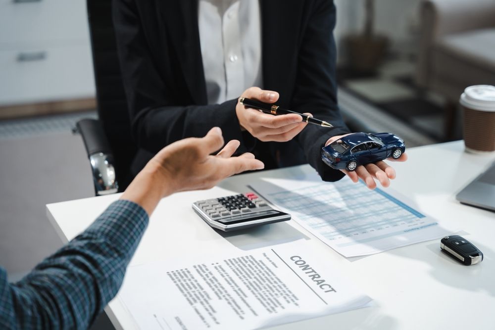 Hands exchanging car keys and documents over a desk during a vehicle sale meeting