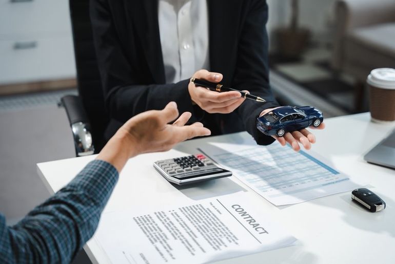 Hands exchanging car keys and documents over a desk during a vehicle sale meeting
