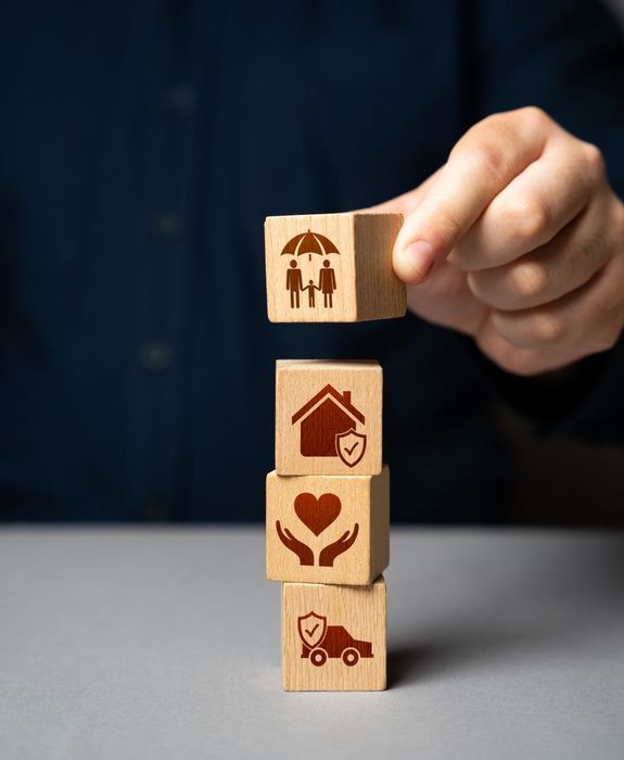 Hand holding stacked wooden blocks with family, home, heart, and insurance icons