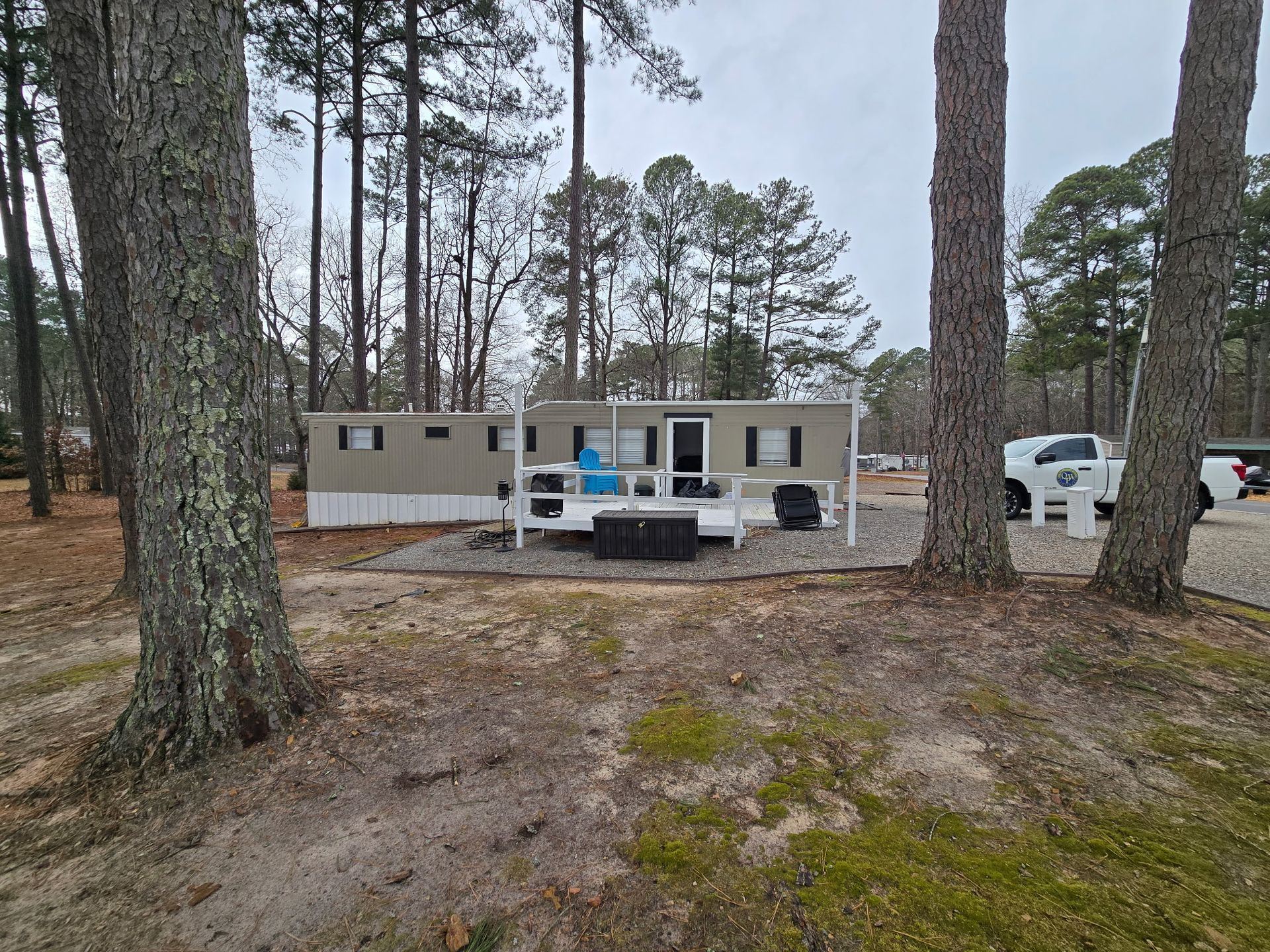 A mobile home with a small porch sits among tall trees on a cloudy day.