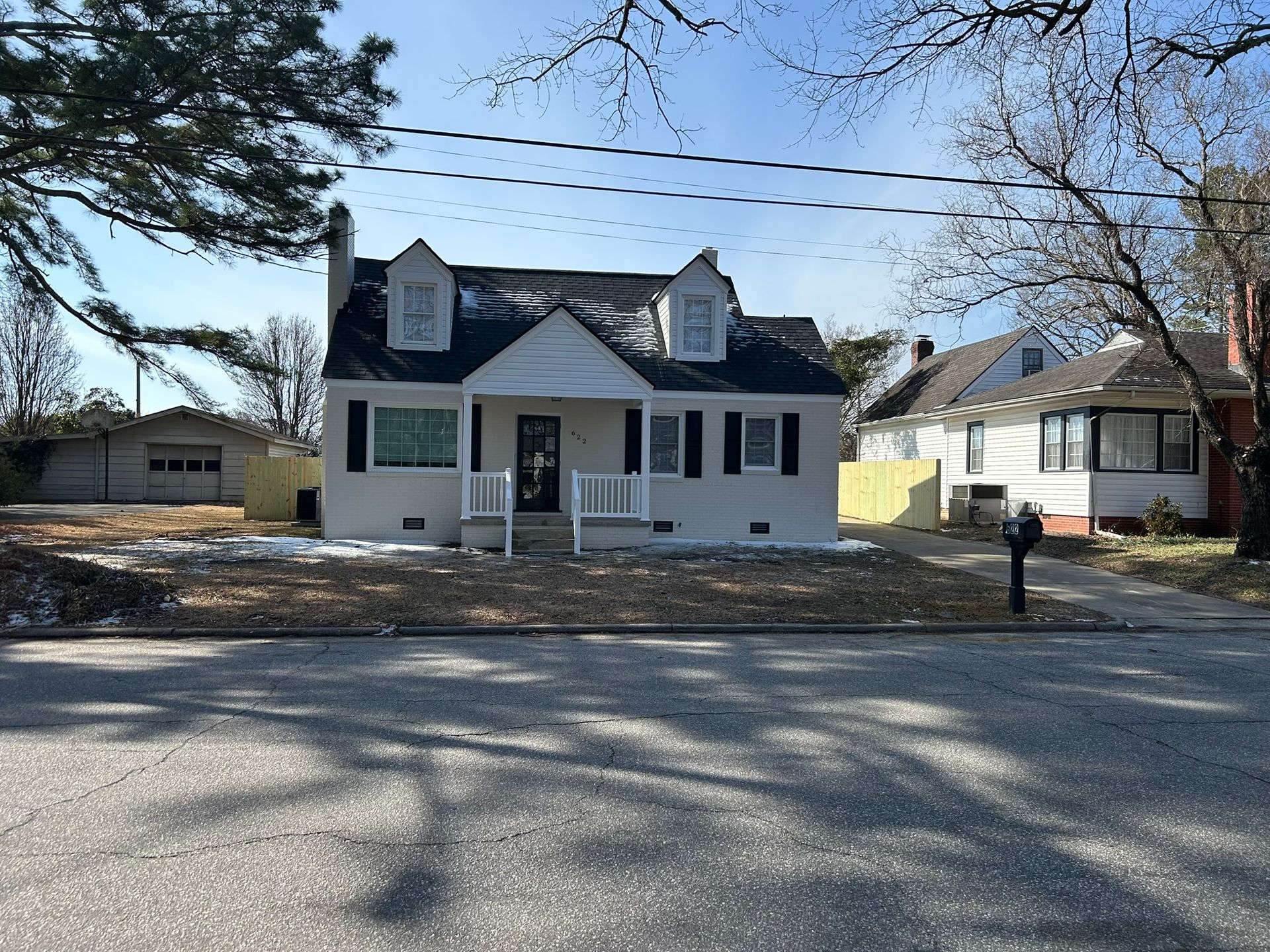 White house with black shutters, dormers, and a small porch on a sunny day.