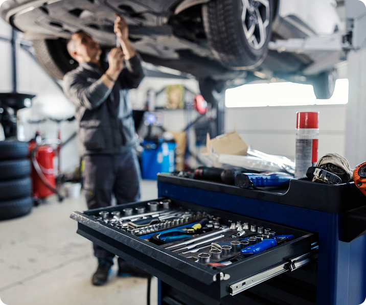 Mechanic working under a raised car beside an open tool chest in an auto repair garage | Godwin Automotive