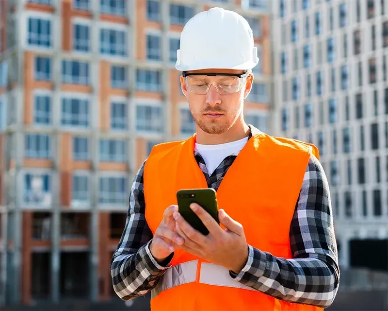 Een bouwvakker gebruikt een mobiele telefoon op een bouwplaats.