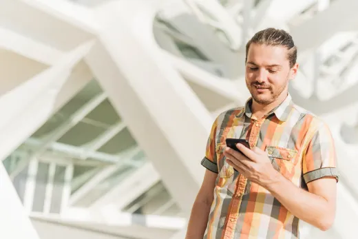 A man is standing in front of a building looking at his cell phone.