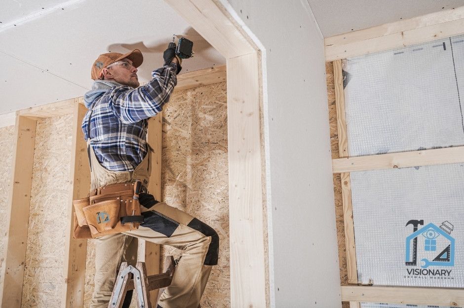 A drywall contractor in Markham, Ontario working off of his ladder installing Sheetrock onto a ceiling using a drill.