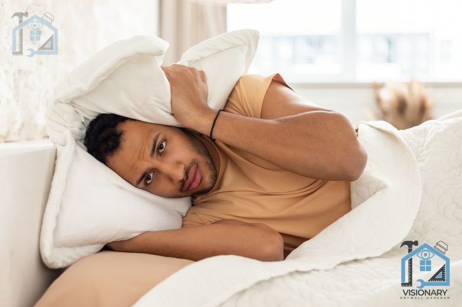 A guy laying down in bed covering his ears with a pillow wishing he had soundproof drywall installed in his Markham, Ontario home.