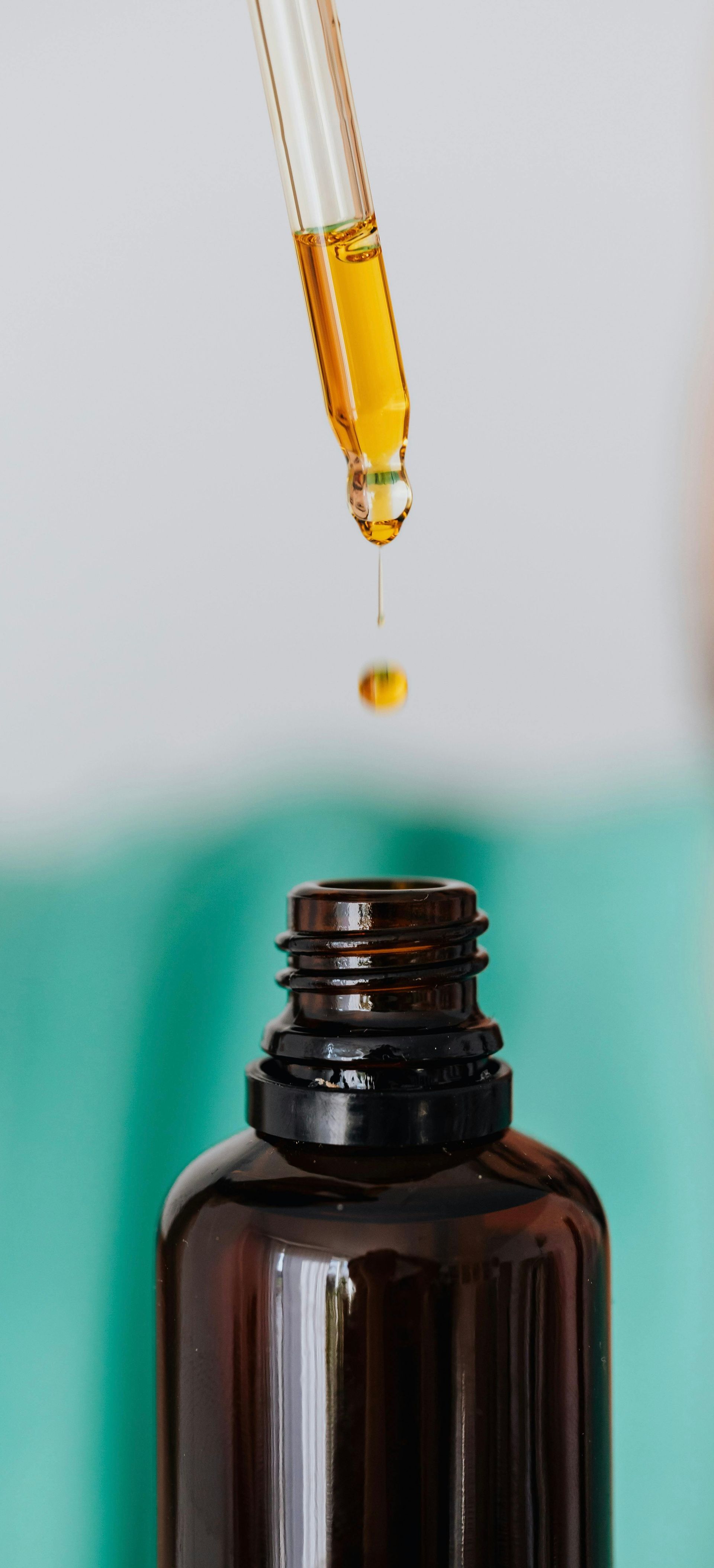 Dropper releasing a drop of amber colored oil into a dark glass bottle.