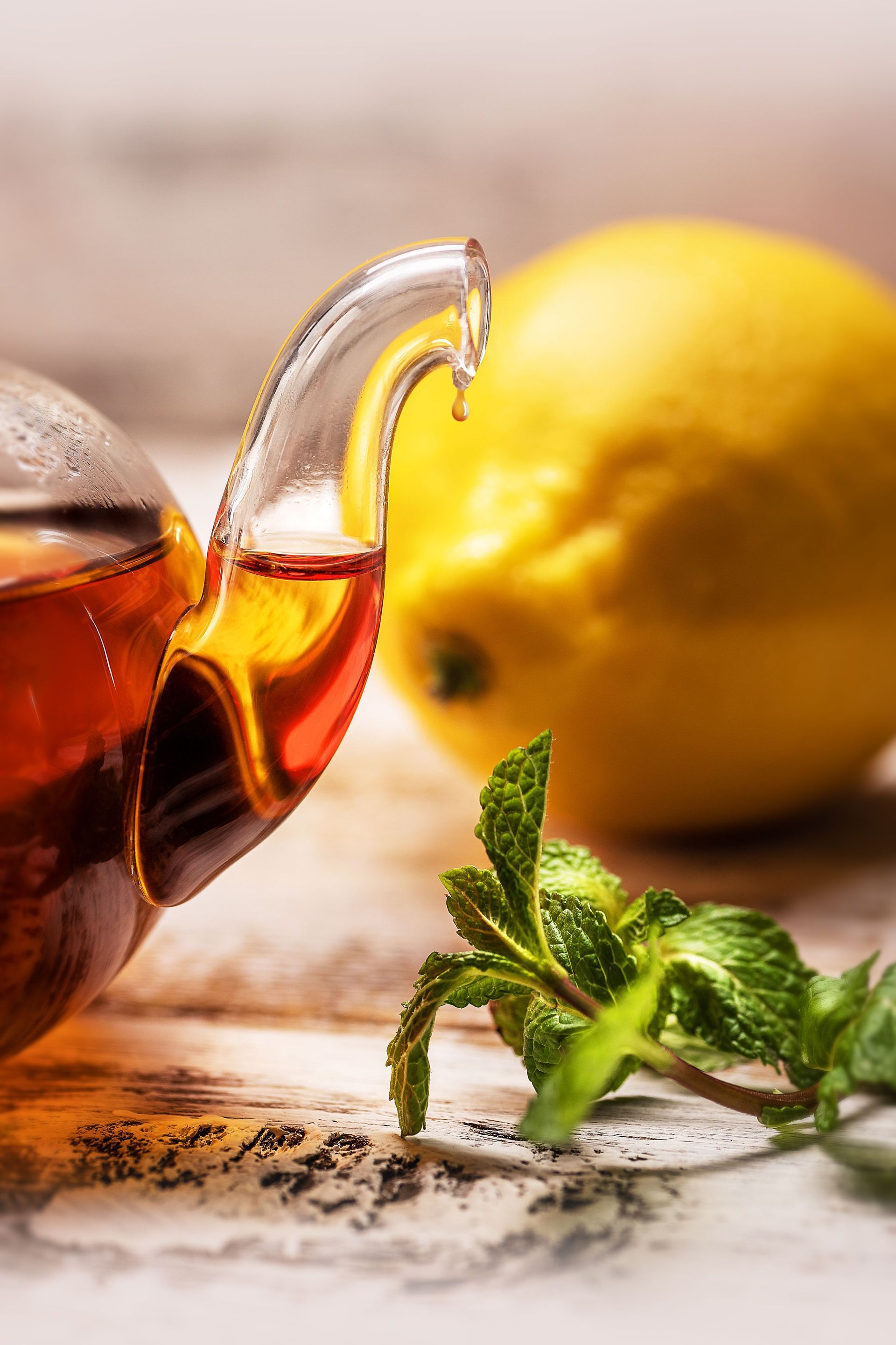 tea pot full of black tea with a lemon in the background and a spring of mint in the foreground