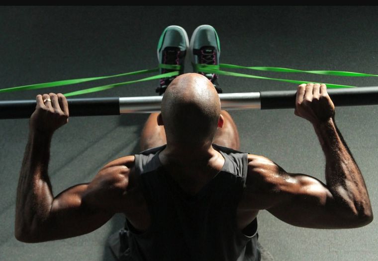 Person doing a weighted pull-up on a bar in a gym, viewed from above, with green resistance bands attached