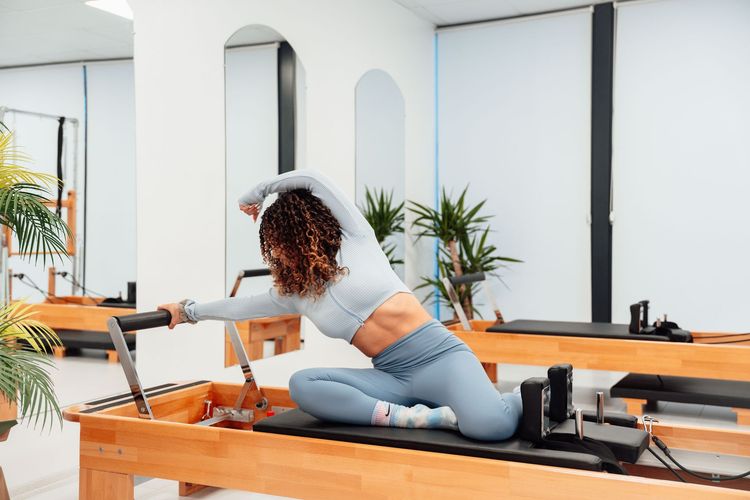 Woman stretching on a Pilates reformer in a bright studio