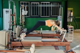 Woman doing Pilates on a reformer in a studio, leaning forward in a plank position