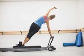 Two athletes in a gym doing overhead squats, one with a barbell and one guiding with a kettlebell overhead