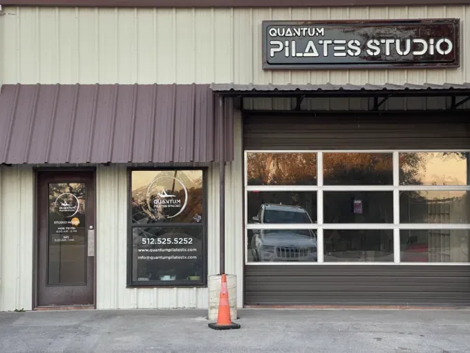 Storefront for Quantum Pilates Studio with a glass door, large window, and orange traffic cone outside.
