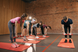 People stretching on yoga mats in a studio with wooden walls and brick backdrop