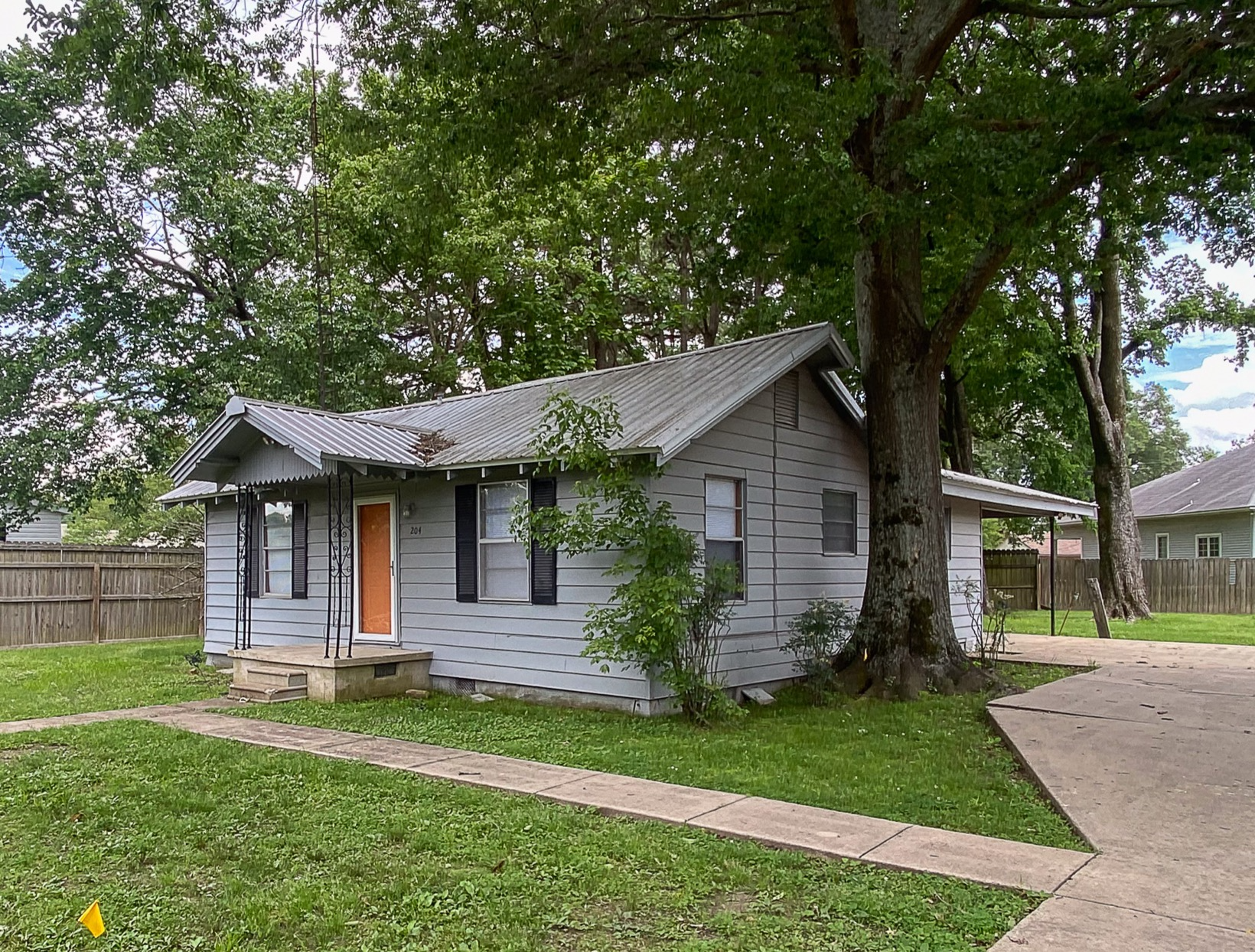 Small gray house with orange door beside a large tree and sidewalk in a grassy yard