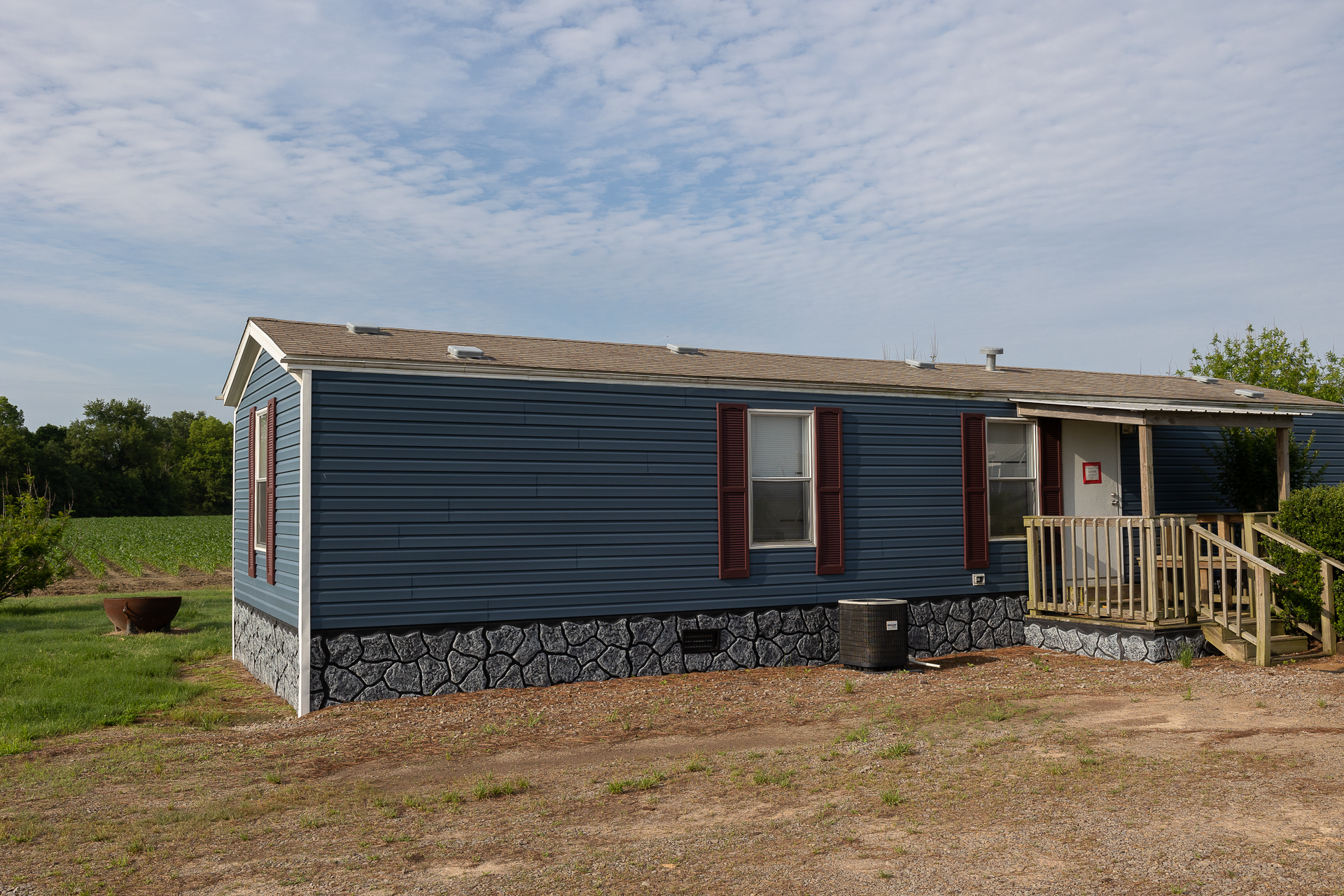 Single-story blue house with a small porch and stone foundation in a rural setting