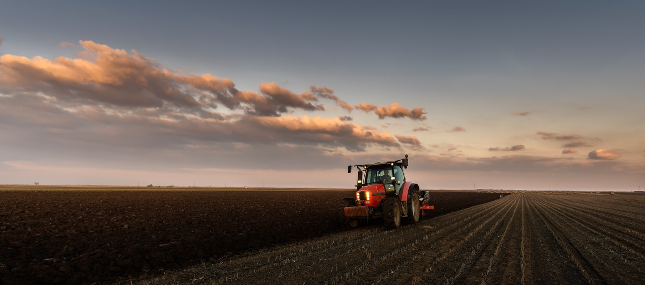 Tractor plowing a dark field at sunset under a cloudy sky