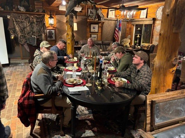 Group dining at a rustic restaurant table with drinks and plates in a warm, wood-paneled room