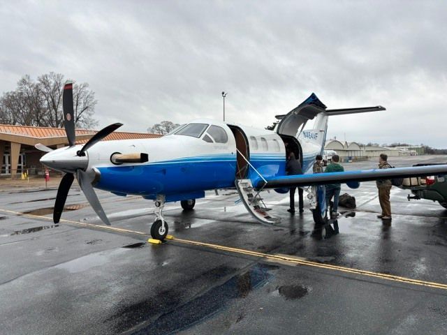 Blue-and-white propeller plane on a wet tarmac with a person boarding via a rear stairway