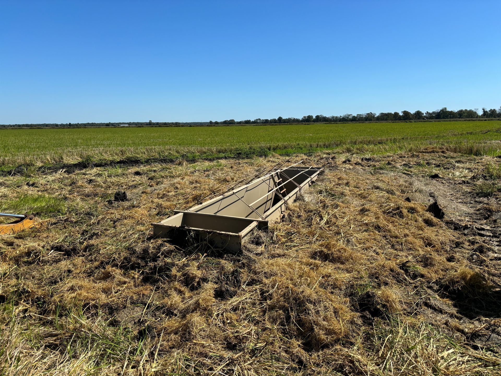 Broken wooden farm feeder lying in a dry field under a clear blue sky
