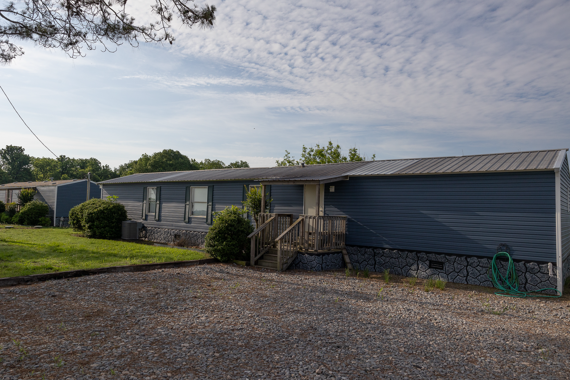 Single-story house with gray siding, gravel driveway, and a small front deck under a cloudy sky