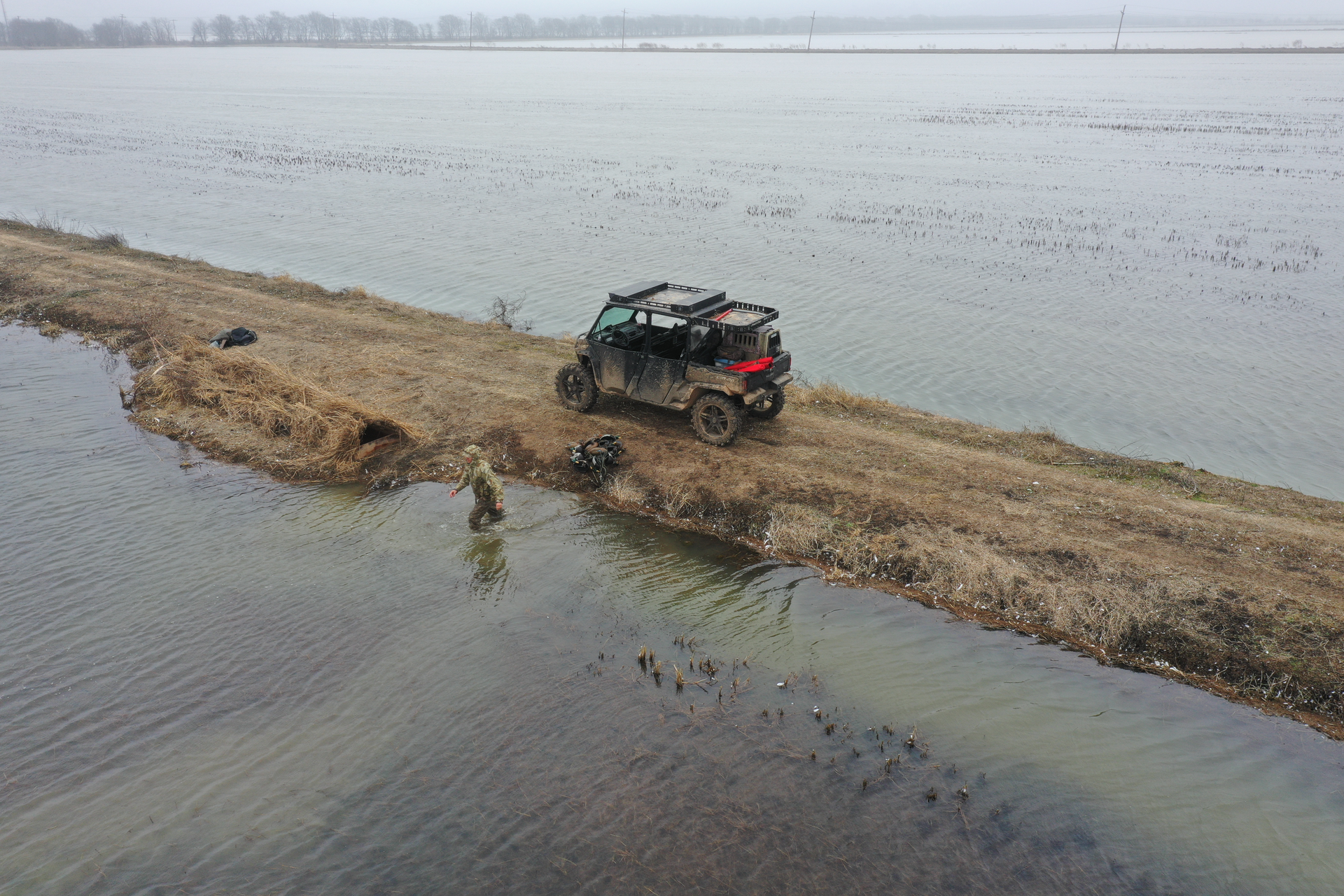 Off-road vehicle on a muddy lakeshore beside shallow water under an overcast sky