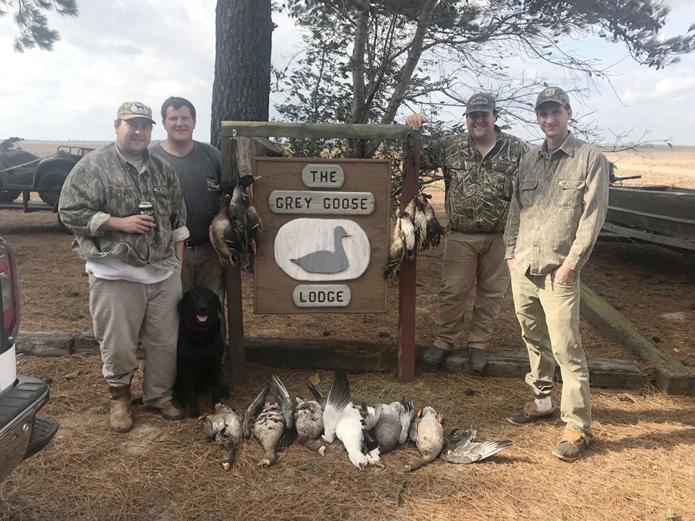 Four hunters posing by a “The Grey Goose Lodge” sign with several geese laid on the ground.
