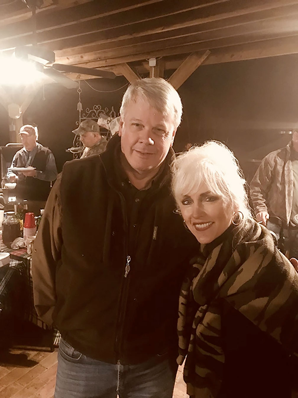 Two people smiling and posing together at a dimly lit indoor gathering.