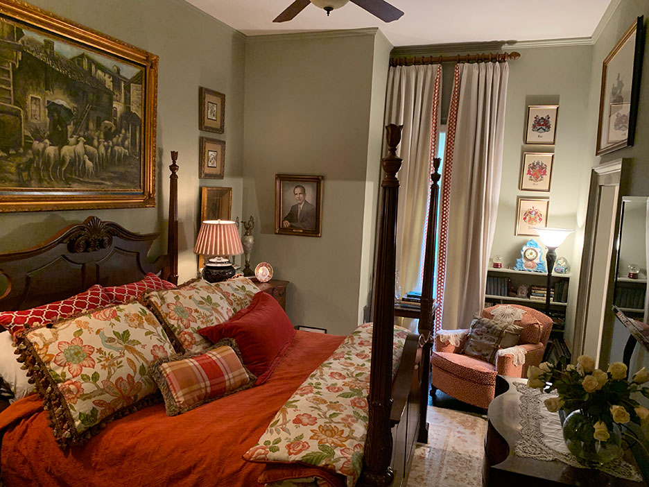 Cozy bedroom with ornate bed, orange bedding, framed art, and a window seat by tall windows