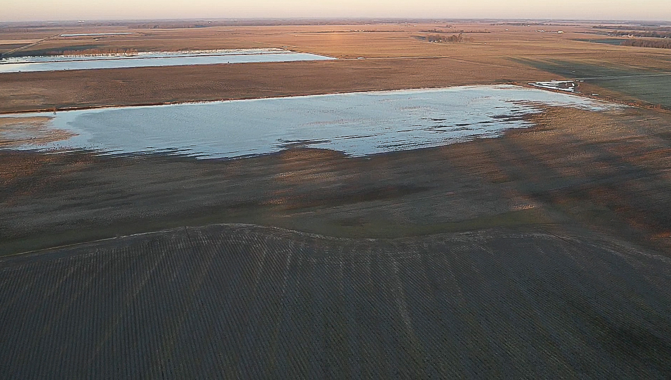 Shallow water pools in a barren, muddy landscape under a wide open sky.