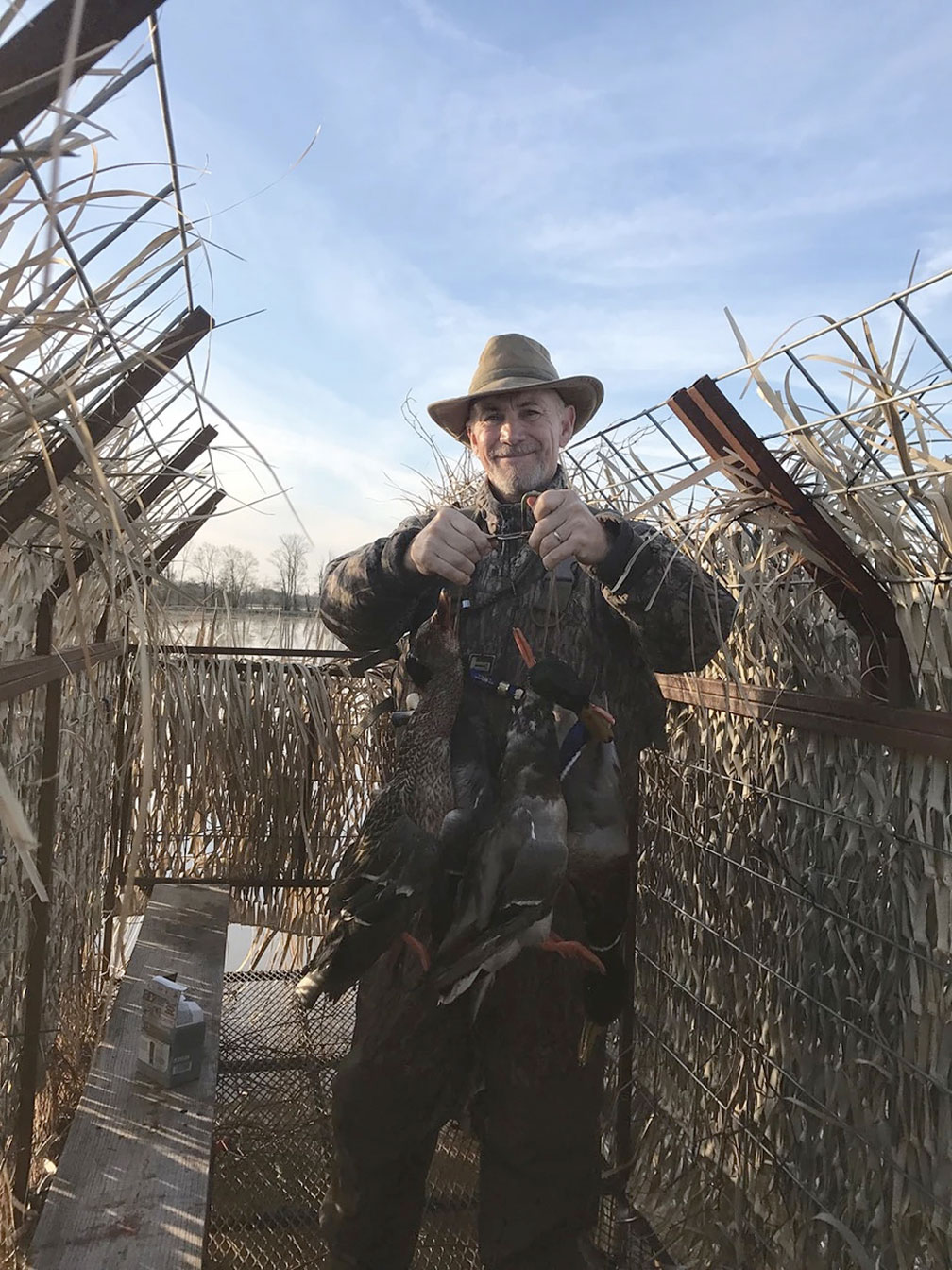 Person in a hat standing outdoors in a woven fence enclosure under a blue sky, holding something in both hands